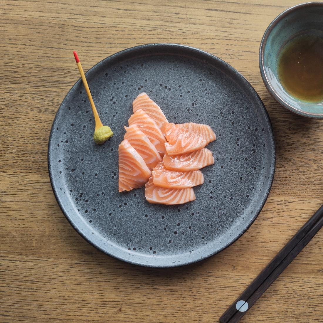 Sliced salmon sashimi arranged on a speckled grey plate